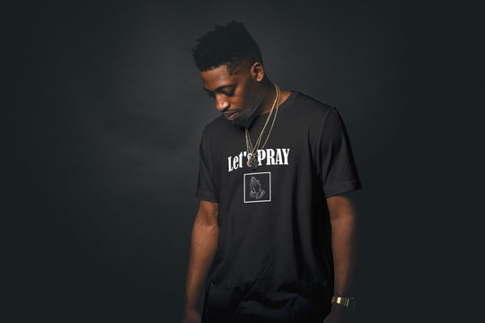 Let's Pray Men T-shirt. T-shirt shows words in white and image of praying hands in a square shape. T-shirt shown in black.